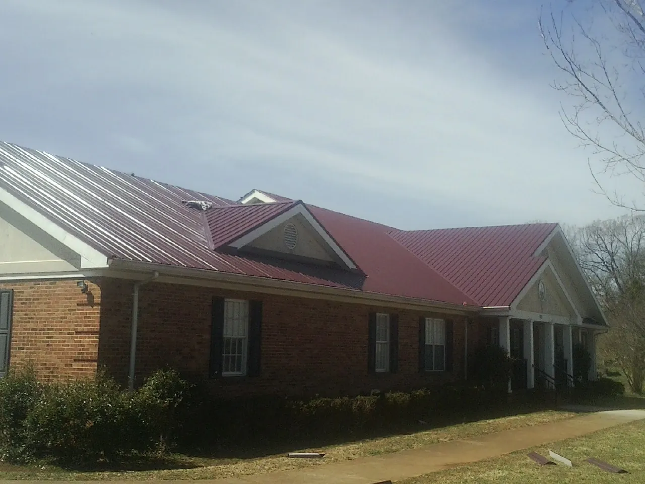 Red metal roof with gabled entries on a long brick building, from a Hail Damage Roof Repair job in Vincent