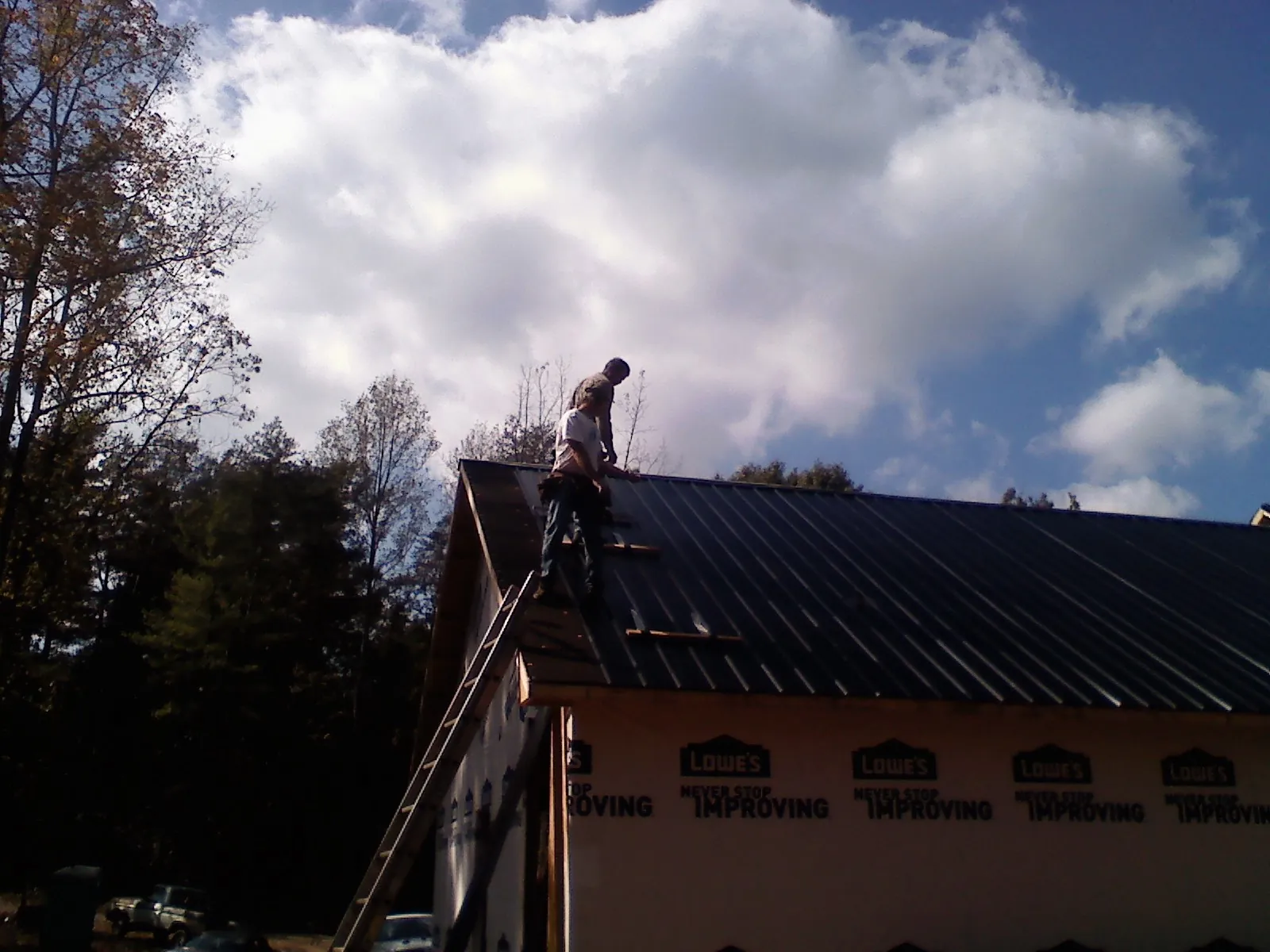 Roofer fastening dark metal panels high against a cloudy sky, from a Roof Inspection job in Vincent