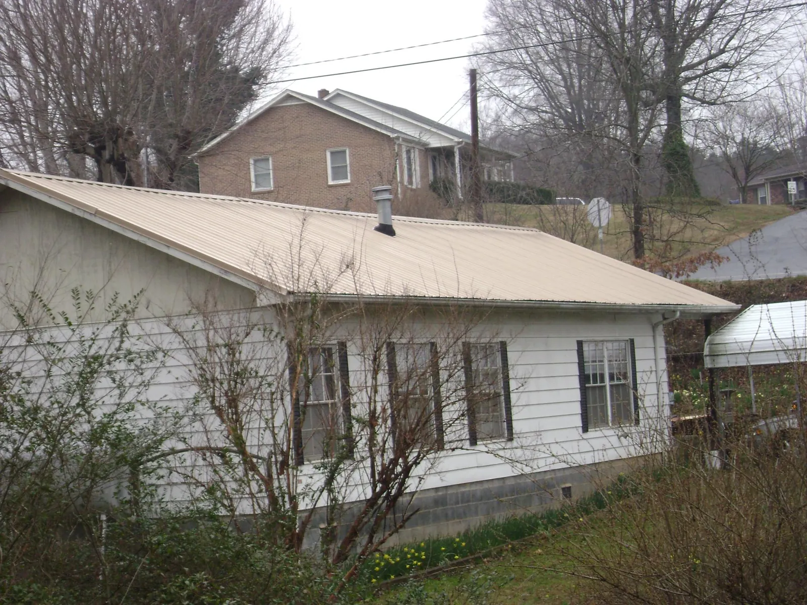 Tan metal roof on a white sided house set into a hillside — Commercial Roofing by Roofing Brothers in Vincent